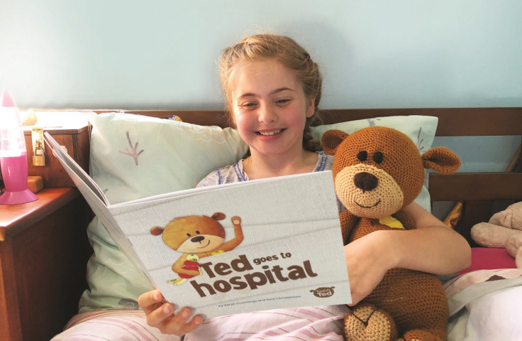Child reading book with teddy in hospital bed